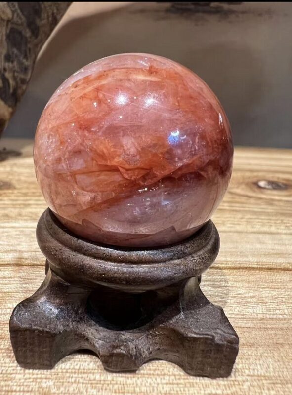 A translucent clear quartz bead displaying natural green chlorite and rust-red hematite inclusions, creating a miniature landscape visible within the crystal