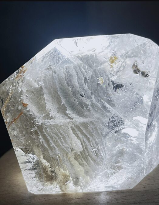 A clear quartz crystal displaying natural white phantom formations within, showing layered white mineral outlines suspended in the crystal body under direct light