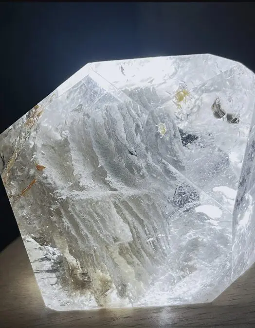A clear quartz crystal displaying natural white phantom formations within, showing layered white mineral outlines suspended in the crystal body under direct light