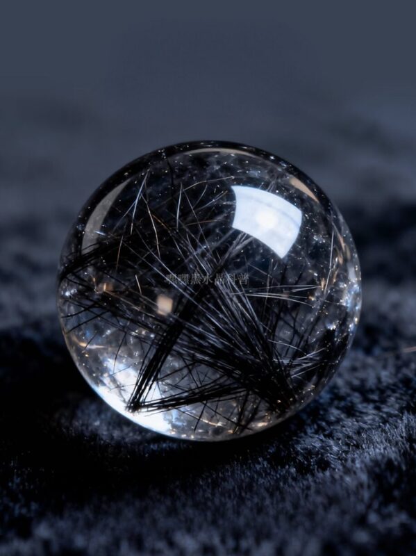 Detail photograph of a Black Rutilated Quartz bead, showing dark needle-like inclusions radiating through translucent quartz, set against a clean minimal background.