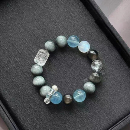 A cool-toned multi gem stretch bracelet in grey-blue and white, featuring hawk's eye, aquamarine, blue tiger's eye, and moonstone beads arranged in a closed circle on a dark background.
