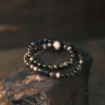 Golden obsidian bead surface detail, polished volcanic black glass with gold-silver chatoyant sheen, characteristic mineral sheen shimmer, polished surface detail