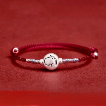 Bracelet laid flat or modeled on wrist against deep burgundy or neutral background; full cord length visible including peace-knot closure and zodiac charm. Alt Text: "Adjustable Chinese red braided cord bracelet with pure silver zodiac charm — Horse design shown