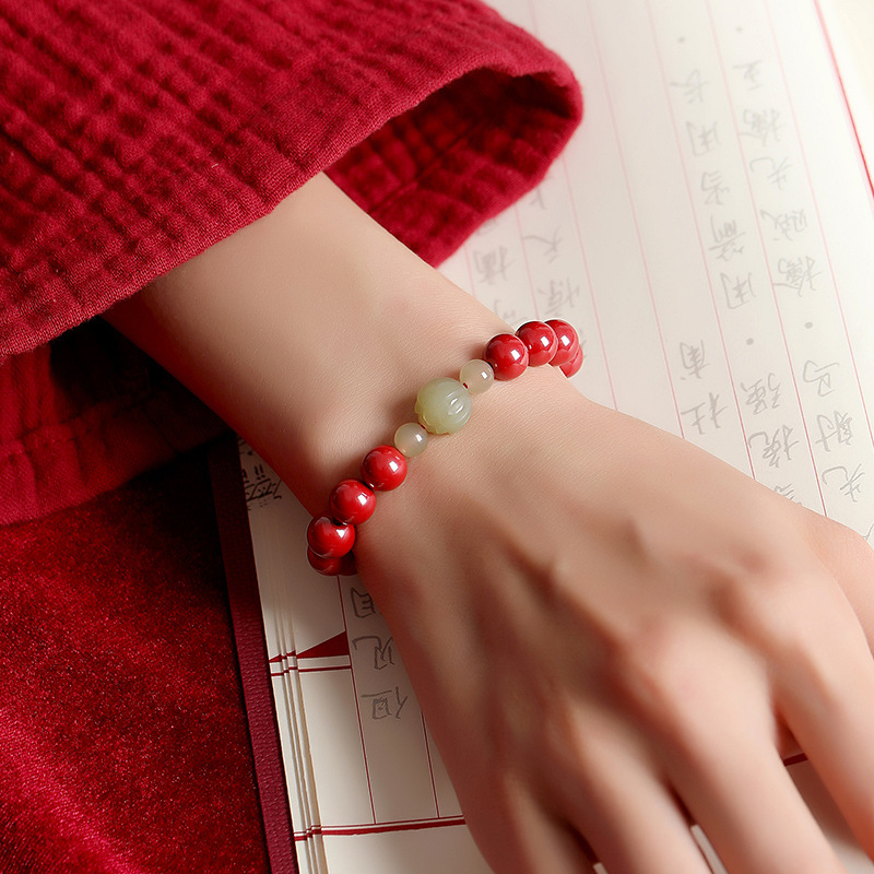 : A woman wearing a cinnabar and Hetian jade lotus bracelet on the wrist, shown in warm natural indoor lighting.