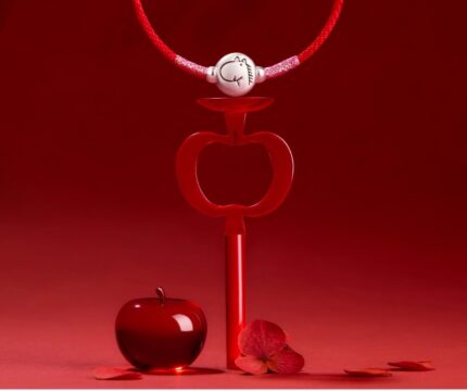 Close-up of peace-knot closure and silver zodiac charm. Alt Text: "Detail of double-bead peace-knot closure and pure silver engraved zodiac charm on red braided cord