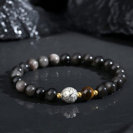Polished black obsidian beaded bracelet with golden Tiger's Eye focal beads and sterling silver koi fish charm, dark background, natural lighting