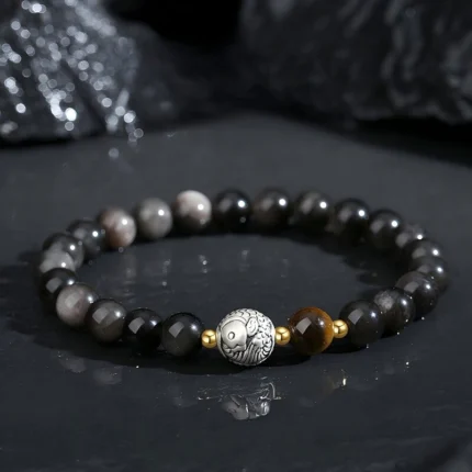Polished black obsidian beaded bracelet with golden Tiger's Eye focal beads and sterling silver koi fish charm, dark background, natural lighting