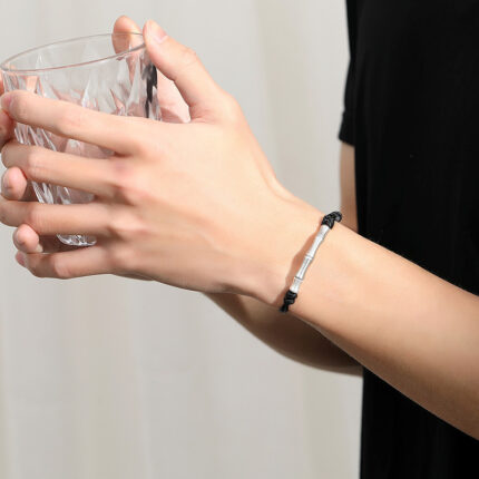 The black braided cord and brushed silver bamboo charm detail on the wrist, showing the lightweight and minimal aesthetic.