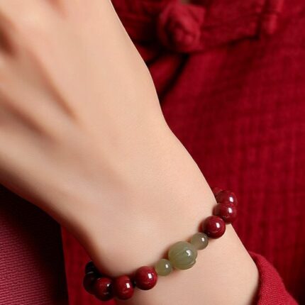 Wrist-shot in natural light showing the weight and presence of the bracelet on the wrist. Evening or warm indoor lighting preferred to show the cinnabar depth.