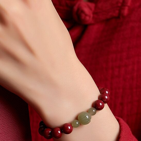 Wrist-shot in natural light showing the weight and presence of the bracelet on the wrist. Evening or warm indoor lighting preferred to show the cinnabar depth.