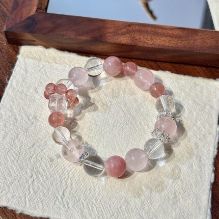 Rose quartz strawberry quartz and clear quartz multi gem bracelet laid flat, 10mm crystal beads in blush pink and ice clear, square-cut clear quartz accent, silver spacer beads, soft natural surface, natural lighting