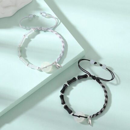 Both bracelets laid flat side by side on a neutral background — black obsidian version on the left, white agate version on the right — showing the bamboo joint beads, white agate peace circles, and silver bamboo leaf pendants clearly.