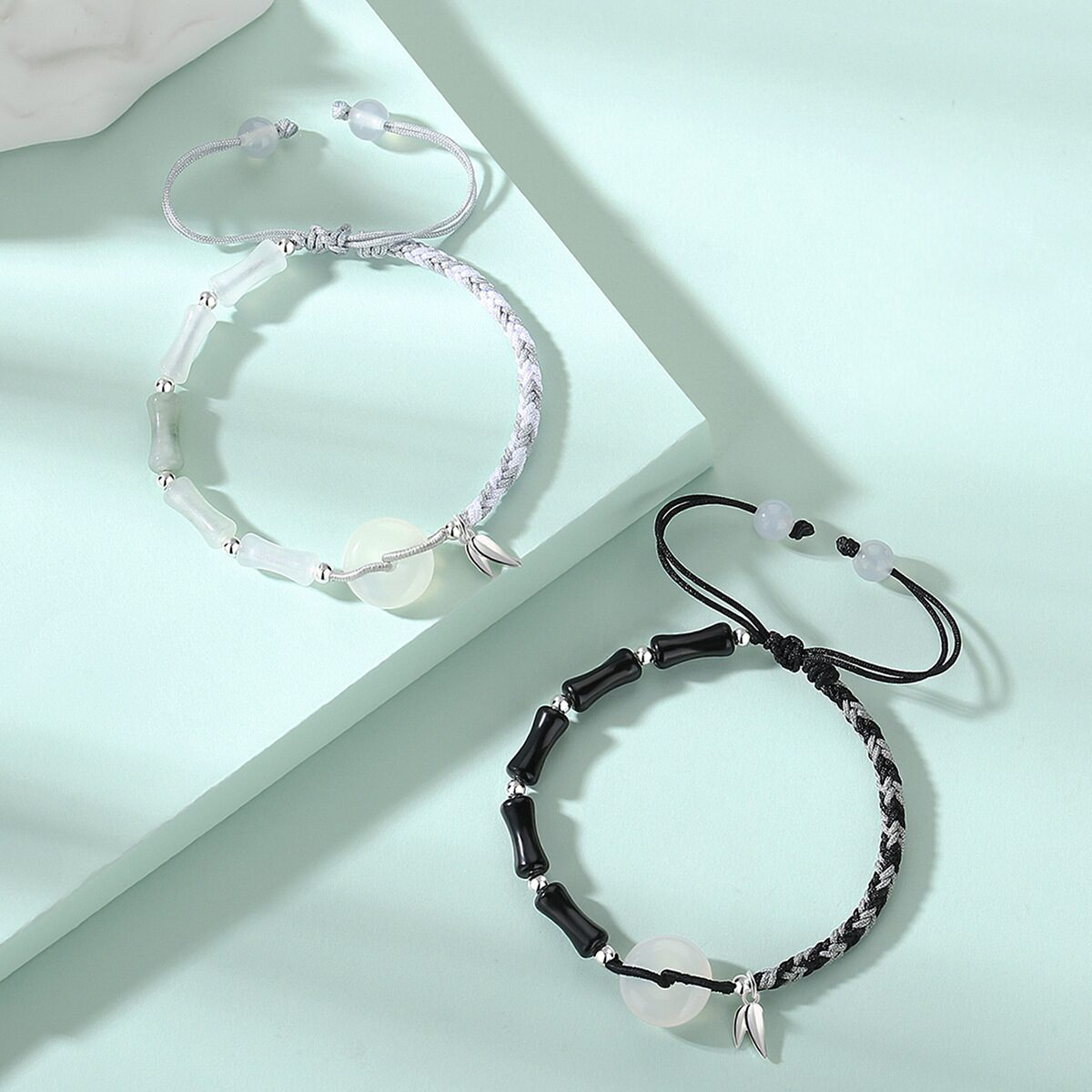 Both bracelets laid flat side by side on a neutral background — black obsidian version on the left, white agate version on the right — showing the bamboo joint beads, white agate peace circles, and silver bamboo leaf pendants clearly.