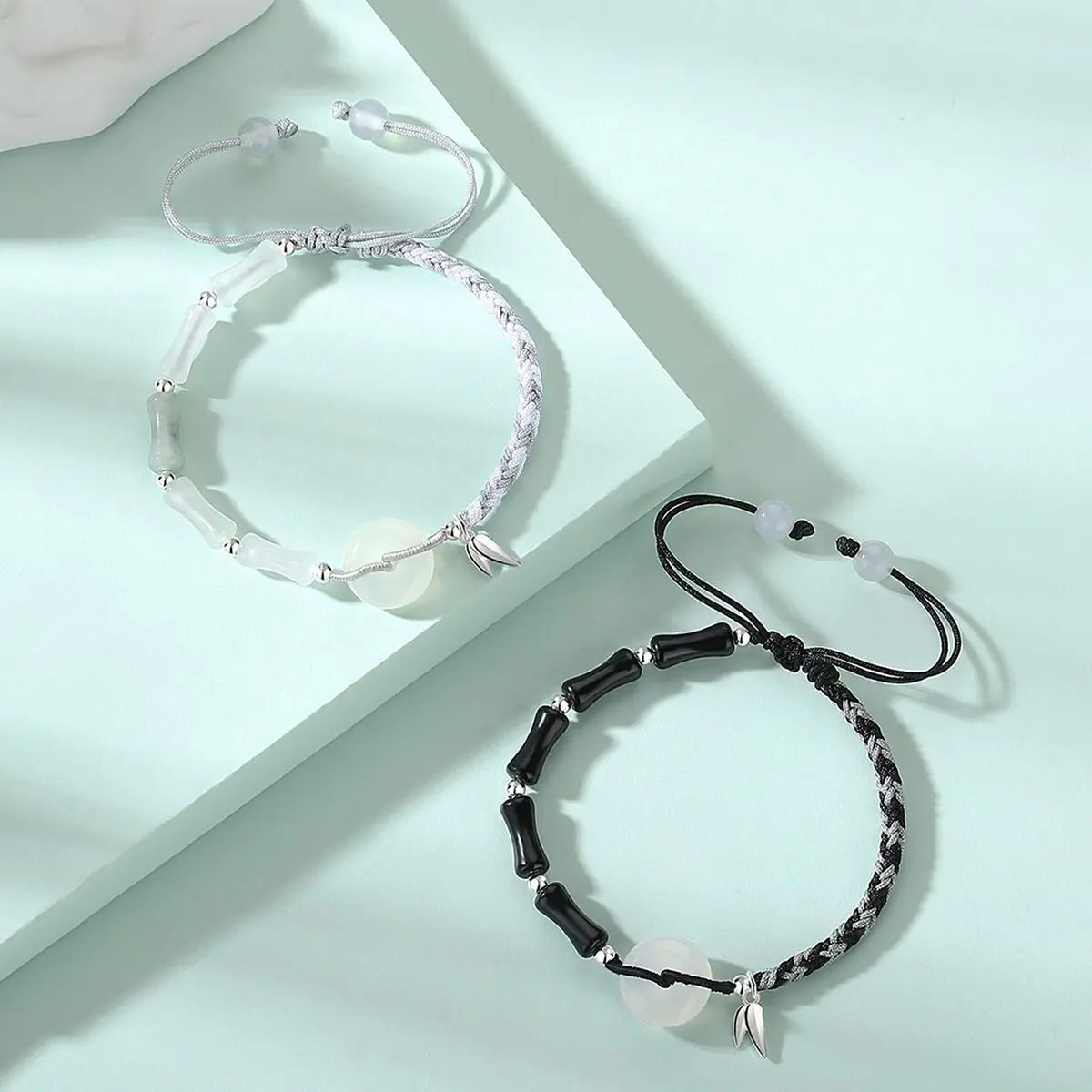 Both bracelets laid flat side by side on a neutral background — black obsidian version on the left, white agate version on the right — showing the bamboo joint beads, white agate peace circles, and silver bamboo leaf pendants clearly.