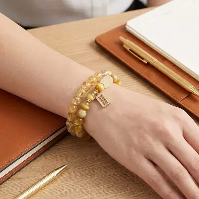 Yellow crystal Pixiu bracelet on wrist beside a cup of tea, soft natural morning light, prosperous and calm atmosphere