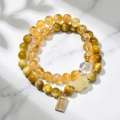 Close-up of yellow rutilated quartz bead showing golden needle-like rutile inclusions inside clear quartz, against neutral background