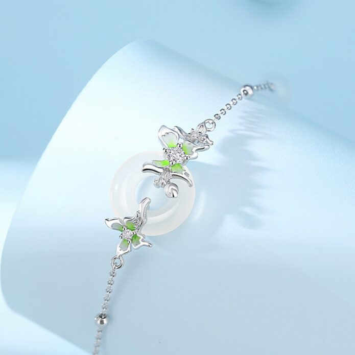 Close-up detail of three S925 silver butterflies with gradient green enamel wings surrounding a polished white agate peace circle pendant