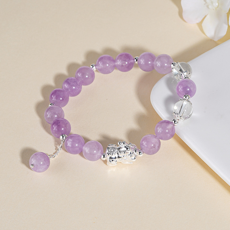 Macro detail of pale lavender amethyst beads and a polished pure silver Pixiu charm on an elastic bracelet.
