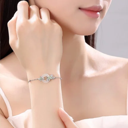 Wrist-shot in natural light — fine silver chain and white agate pendant visible, butterflies catching light. Simple, neutral setting.