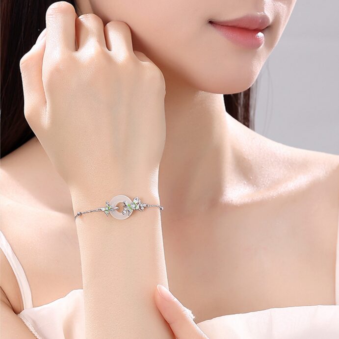 Wrist-shot in natural light — fine silver chain and white agate pendant visible, butterflies catching light. Simple, neutral setting.